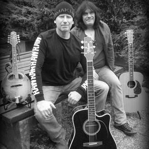 Das Duo McCarthy/Antemann auf einer Bank mit Gitarren