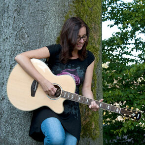 Petra Halfmann mit Gitarre vor einem Baum